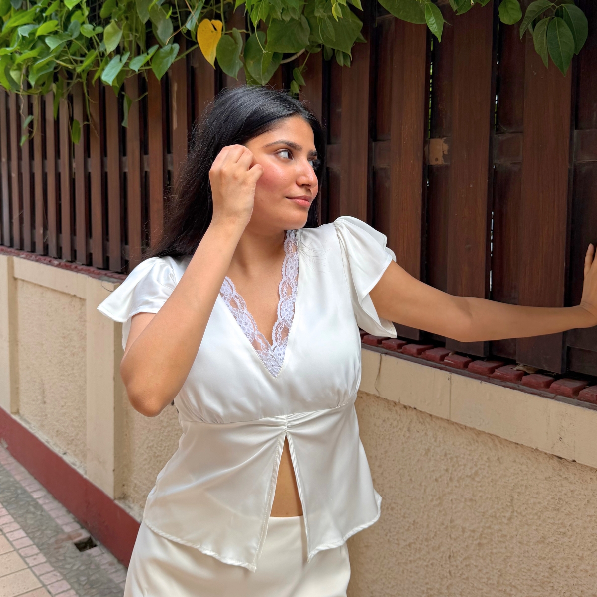 Model wearing Pearl, an off-white satin top with lace neckline and flutter sleeves